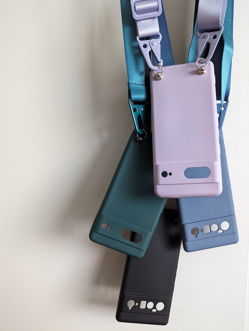 Pu&ograve; includere: Quattro custodie per telefono di diversi colori con cinturini appesi a un muro bianco. Le custodie sono turchese, viola, blu e nero.