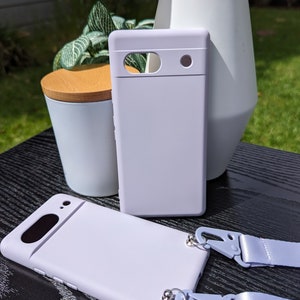 May include: Two lavender phone cases with a matching lavender phone strap. The phone cases have a raised camera bump and a smooth finish.