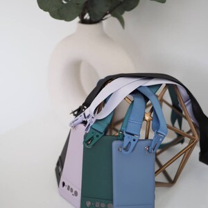 Pu&ograve; includere: Quattro custodie per telefono con cinturini di diversi colori. Le custodie sono lavanda, verde e blu. I cinturini sono neri, bianchi e blu. Le custodie sono su un supporto in metallo dorato.
