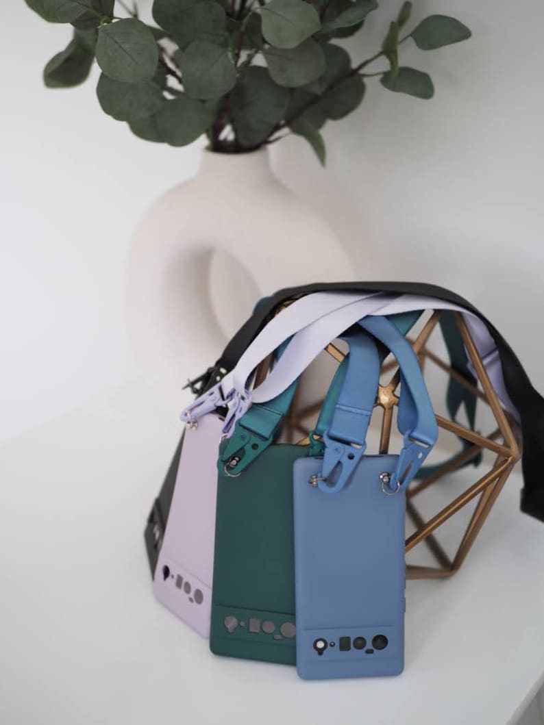 Pu&ograve; includere: Quattro custodie per telefono con cinturini di diversi colori. Le custodie sono lavanda, verde e blu. I cinturini sono neri, bianchi e blu. Le custodie sono su un supporto in metallo dorato.