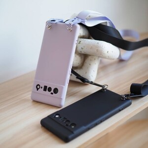 Pu&ograve; includere: Due custodie per telefono con cinturini neri. Una custodia &egrave; lavanda e l'altra &egrave; nera. Entrambe le custodie hanno un ritaglio per l'obiettivo della fotocamera e un piccolo cerchio nero sul retro.