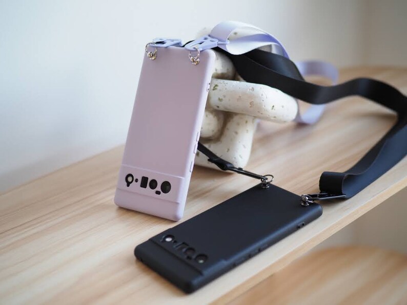 Pu&ograve; includere: Due custodie per telefono con cinturini neri. Una custodia &egrave; lavanda e l'altra &egrave; nera. Entrambe le custodie hanno un ritaglio per l'obiettivo della fotocamera e un piccolo cerchio nero sul retro.