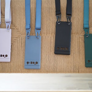 Pu&ograve; includere: Quattro custodie per telefono con cinturini di diversi colori e uno schema di colori bianco, blu, nero e verde. Ogni custodia ha il testo "P-H-O-N-E" stampato.
