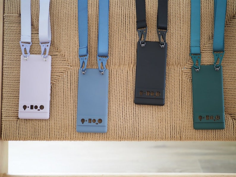 Pu&ograve; includere: Quattro custodie per telefono con cinturini di diversi colori e uno schema di colori bianco, blu, nero e verde. Ogni custodia ha il testo "P-H-O-N-E" stampato.