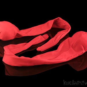May include: Bright red fabric headbands with rounded ends, lying on a reflective black surface. The headbands are soft and appear to be made of a lightweight material. The overall design is simple and elegant.
