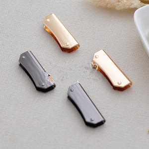 May include: Four metal clasps, two gold and two black, with a rounded rectangular shape and a small raised dot on each end.