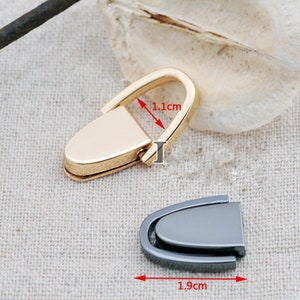 以下が含まれることがあります： 2つの金属製バッグ留め具。1つは金色で幅1.1cm、もう1つはグレーで長さ1.9cmです。どちらもカーブしたデザインで、ヒンジ開閉式で、バッグやアクセサリーに適しています。