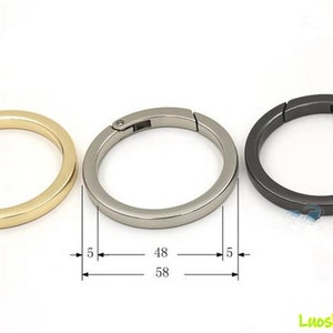Puede incluir: Tres anillos redondos de metal con resorte en dorado, plateado y gris oscuro. Los anillos tienen 5 mm de grosor, con un diámetro exterior de 58 mm y un diámetro interior de 48 mm. Los anillos se abren y cierran con un mecanismo de resorte.
