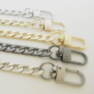 May include: Close-up of four metal chain straps in silver, gold, gunmetal, and light silver. Each chain has a lobster clasp at the end. The chains are made of thick, interlocking links.