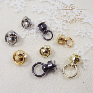 Puede incluir: Una colección de herrajes metálicos para bolsos en varios acabados, incluyendo plata, oro y negro. Los herrajes presentan un anillo y una parte superior decorativa, adecuados para la fabricación de bolsos y proyectos de artesanía.