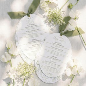 Pode incluir: Dois menus ovais com laços de fita verde, com escrita elegante e detalhes florais. Os menus, intitulados "Rocky" e "Bernadette", são rodeados por flores brancas e vegetação, criando uma estética suave e romântica.