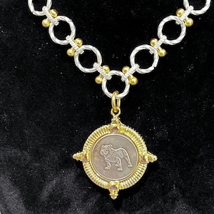 May include: A silver and gold chain necklace with a round pendant featuring a bulldog silhouette. The pendant is surrounded by a gold frame with decorative accents.
