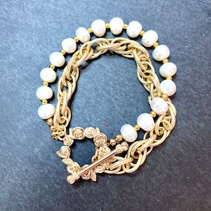 May include: A gold chain bracelet with a rose-shaped clasp and a strand of white pearls.