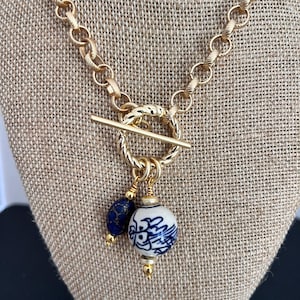 May include: Gold chain necklace with a toggle clasp and a blue and white porcelain pendant with a gold accent.