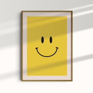 Op de afbeelding: Een ingelijst print met een gele achtergrond en een zwart smiley-gezicht.