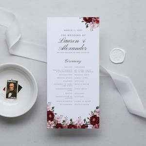 May include: A wedding ceremony program with a floral design featuring burgundy and pink flowers. The program lists the order of events for the wedding of Lauren & Alexander on March 11, 2023.