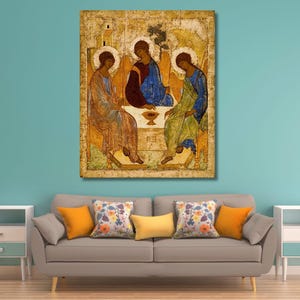 May include: A rectangular wall art print featuring a reproduction of the Rublev Trinity icon, depicting three figures with halos seated around a table with a chalice, rendered in shades of gold, blue, and green on a textured, aged-looking background.