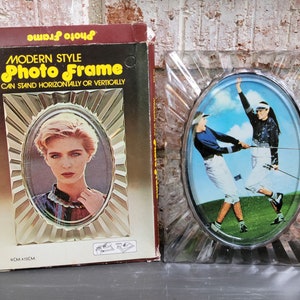 May include: A vintage photo frame with a modern style design. The frame is made of clear plastic and has a silver-colored border. The frame can stand horizontally or vertically. The packaging shows a woman in a photo frame and the text "Modern Style Photo Frame Can Stand Horizontally or Vertically".