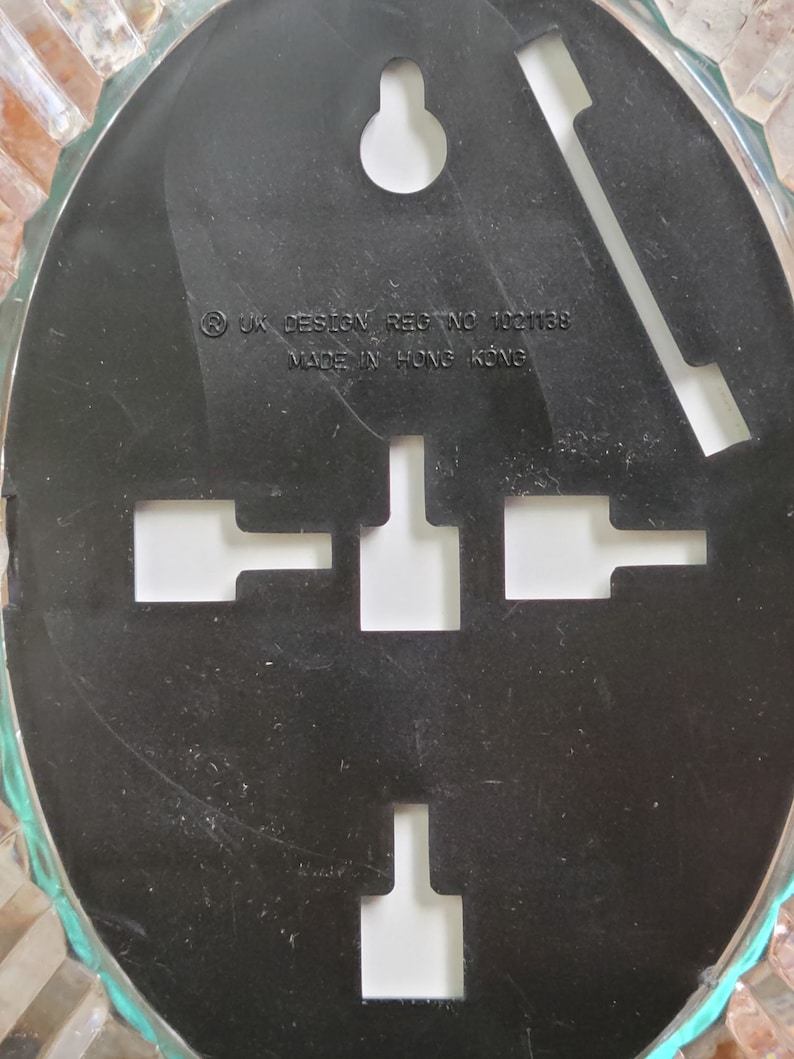 May include: Black oval-shaped wall hanging with a textured surface. It has a hole at the top for hanging and four cut-out shapes in the center. The text on the back reads "UK DESIGN REG NO 1001138 MADE IN HONG KONG".