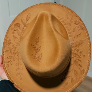 May include: A brown felt fedora hat with a floral design embroidered around the brim.