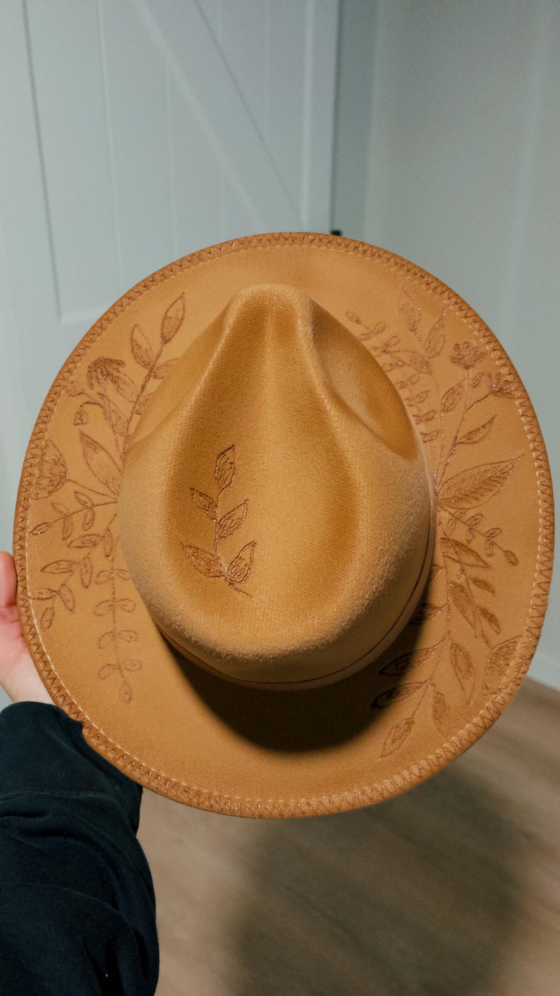 May include: A brown felt fedora hat with a floral design embroidered around the brim.