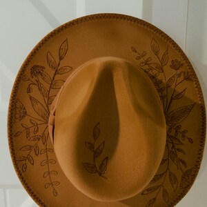May include: A brown felt fedora hat with a stitched brim and a floral design. The hat has a wide brim and a tall crown.