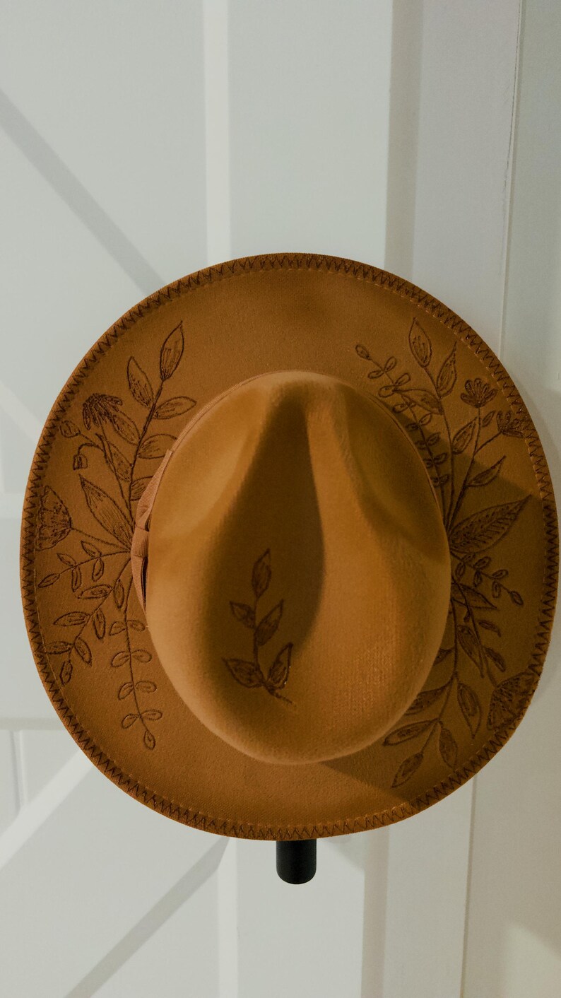 May include: A brown felt fedora hat with a stitched brim and a floral design. The hat has a wide brim and a tall crown.