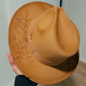 May include: A brown felt fedora hat with a floral design embroidered around the brim.