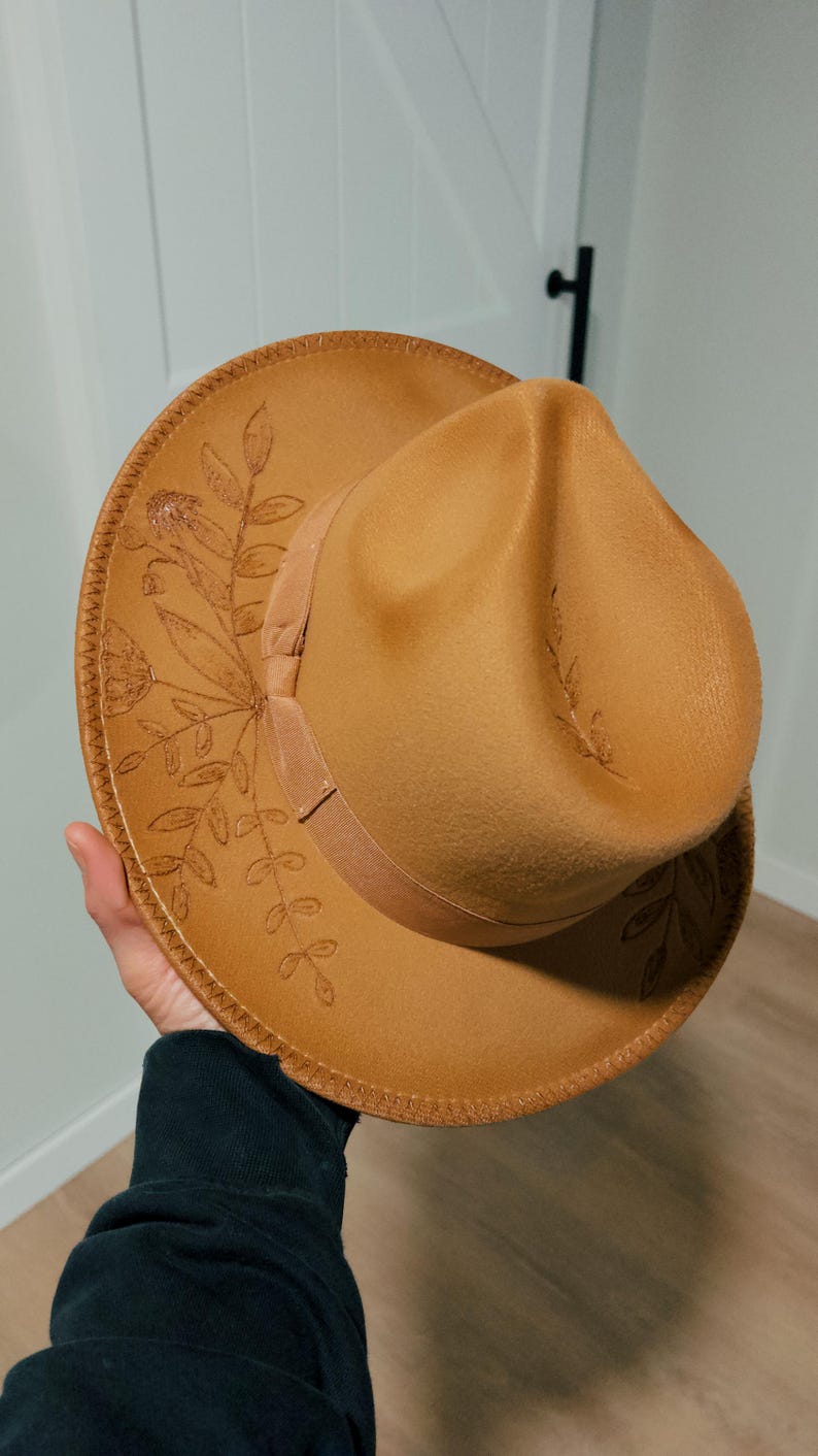May include: A brown felt fedora hat with a floral design embroidered around the brim.