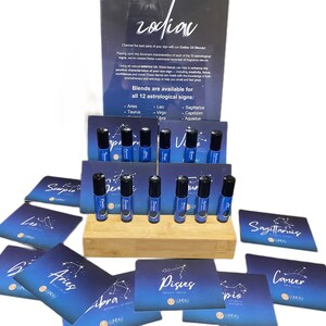 May include: A display of Zodiac Oil Blends, featuring twelve small blue bottles with black caps, arranged on a wooden stand. Each bottle is labeled with a zodiac sign. Cards with zodiac constellations are also visible.