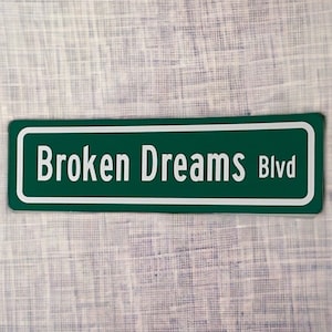 May include: A green street sign with white lettering that reads "Broken Dreams Blvd."