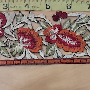 May include: Embroidered floral trim featuring red, orange, and white flowers with green leaves. The trim is approximately 10 inches long and has a decorative border. Ideal for embellishing garments or craft projects.