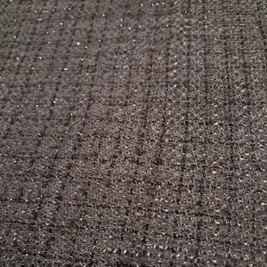 May include: A dark gray fabric with a visible woven grid pattern and a subtle metallic shimmer throughout the material. The textile features a textured surface with intersecting horizontal and vertical threads creating a consistent square weave design.