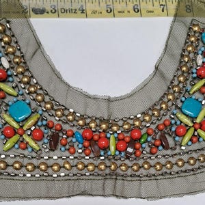 May include: Embellished neckline applique with a variety of colorful beads and stones. The design features red, turquoise, yellow, and brown beads, and gold-colored metal beads, all set on a sheer, gray mesh backing.