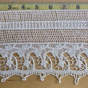 May include: An off-white lace trim featuring a grid-like pattern at the top and a floral scalloped edge at the bottom. A yellow measuring tape is visible along the top and left side, showing a width of approximately 11 inches and a height of 5 inches.