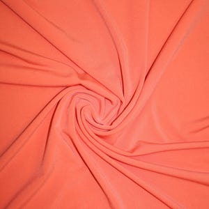 May include: A close-up of a coral-colored fabric with a smooth, silky texture. The fabric is draped and folded, creating a soft, flowing effect.