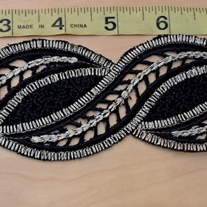 May include: Black and silver decorative trim with a repeating wave pattern. The trim is approximately 1.5 inches wide and features a detailed design with silver accents. The trim is measured against a ruler.