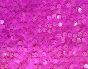May include: A close-up of a bright pink fabric covered in small, round sequins.