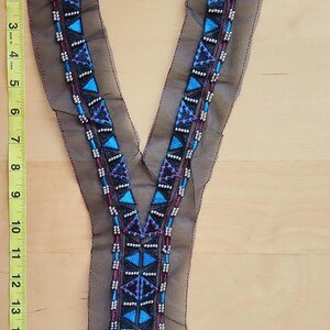 May include: A V-shaped embroidered collar with a black mesh base. The collar features geometric patterns in blue, black, and white beads, with a total length of approximately 10 inches. The design includes triangles and vertical lines.