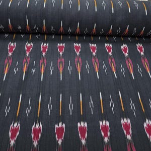 May include: A bolt of dark charcoal gray fabric featuring a repeating ikat pattern. The design consists of vertical rows of stylized, flame-like motifs in shades of deep magenta, bright orange, and white, arranged in a consistent, symmetrical layout.