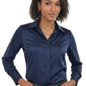 May include: A long-sleeved navy blue button-down shirt with a smooth, satin-like finish, a classic collar, and a concealed front placket. The shirt is paired with a dark grey denim belt featuring a rectangular gold-toned metal buckle.