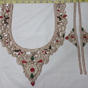 May include: A gold-toned embroidered neckline applique with red and green fabric accents, measuring approximately 13 inches wide and 12 inches long, accompanied by two matching vertical trim strips, all displayed against a white fabric background.