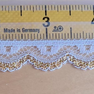 May include: A delicate, light blue lace trim with a scalloped edge and gold metallic thread accents. The trim is approximately 1 inch wide and is shown against a ruler for scale.