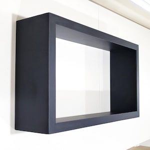 May include: A black floating shelf with a rectangular opening. The shelf is made of wood and has a smooth finish.