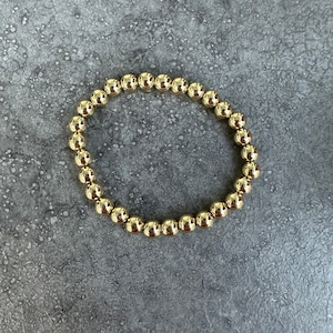 Pode incluir: Um bracelete de contas douradas com um design simples. O bracelete é feito de pequenas contas redondas que são enfiadas em um cordão fino.