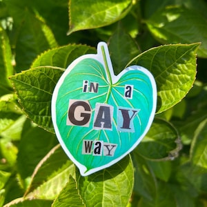 May include: A leaf-shaped sticker with the text "in a GAY way" in a collage style. The sticker is green and teal with a white border, set against a backdrop of green leaves.