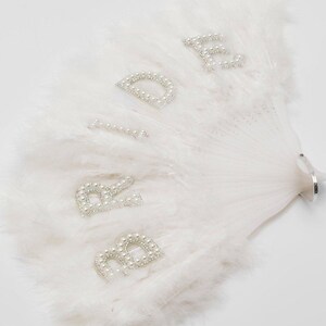 May include: White feather bridal fan with the word "Bride" spelled out in pearl-embellished letters.