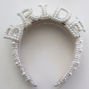 May include: White pearl headband with the word "Bride" spelled out in large pearl letters.