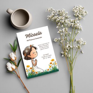 May include: A rectangular card featuring the name Micaela and the text Mi Primera Comuni&oacute;n, with an illustration of a person praying in a field of yellow flowers. The card includes additional Spanish text and the date 08-12-2025.