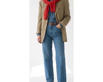 May include: A tan blazer with a subtle brown check pattern worn over a blue denim button-down shirt and blue denim jeans. A bright red sweater is draped over the shoulders. The outfit includes a brown leather belt and brown leather loafers.